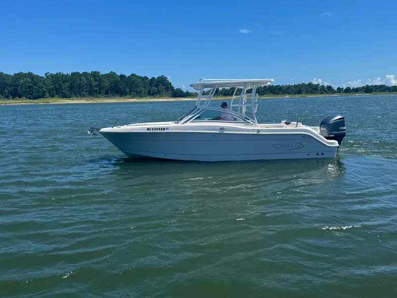 Slide: The Image of 2021 Robalo R247 boat cruising on a sunny day, with lush green shoreline in the background. - 4