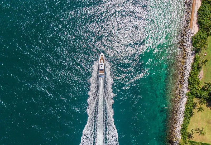 Slide: The Image of Aerial view of 2020 HCB 53 boat cruising on turquoise water near rocky shoreline. - 46