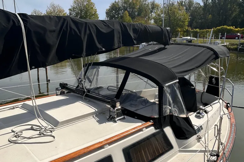 Slide: The Image of 1982 S2 11.0 A sailboat with black canvas cover, docked by a calm river. - 6