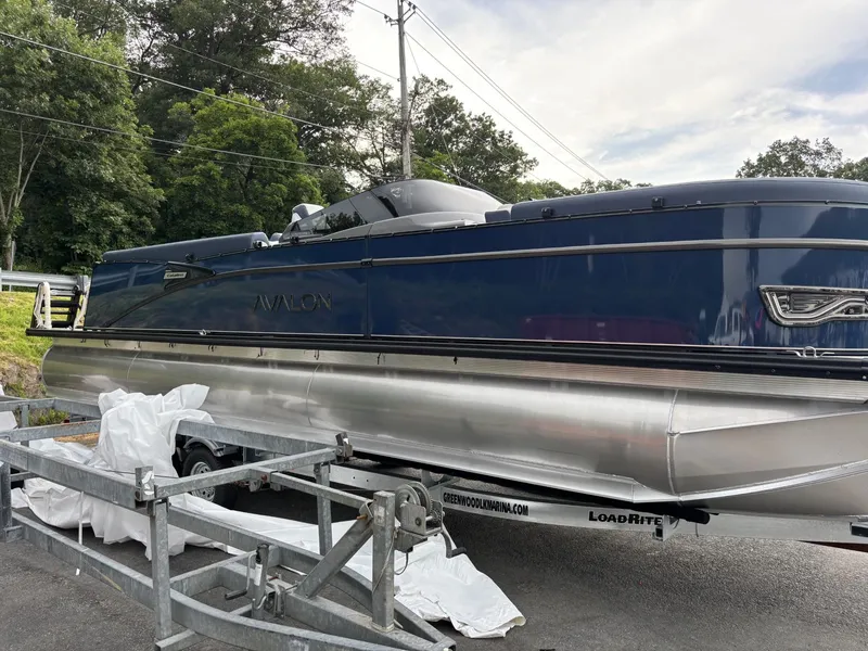 Slide: The Image of 2025 Avalon Catalina Quad Lounger Windshield pontoon boat on trailer, parked outdoors. - 2