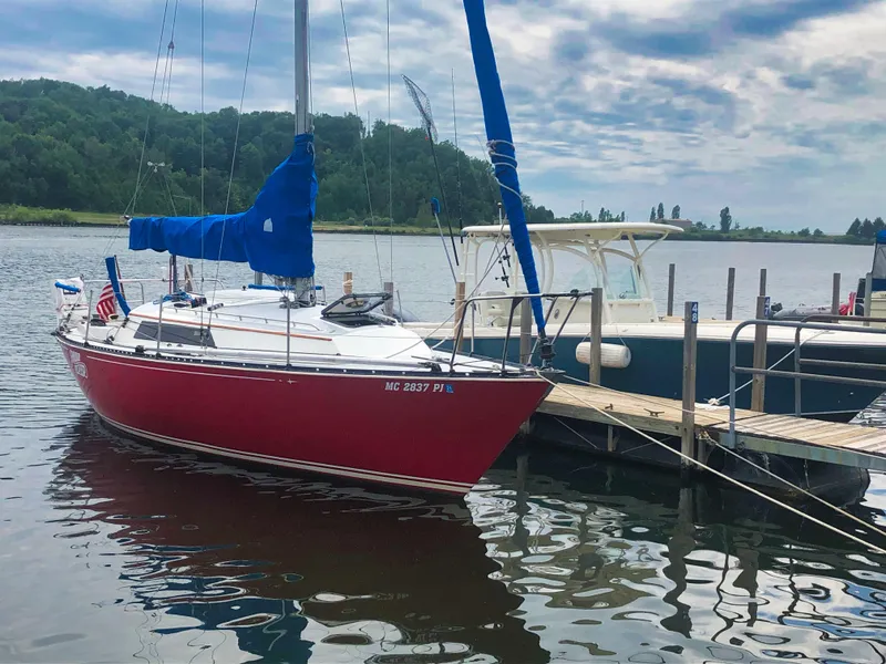 The Image of Red 1979 C&C 29 sailboat docked on a calm lake under a cloudy sky. - 0