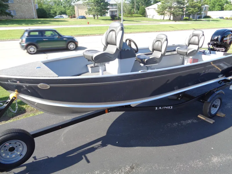 Slide: The Image of 2025 Lund 1600 Fury SS boat on trailer, parked on driveway, with car passing by. - 2