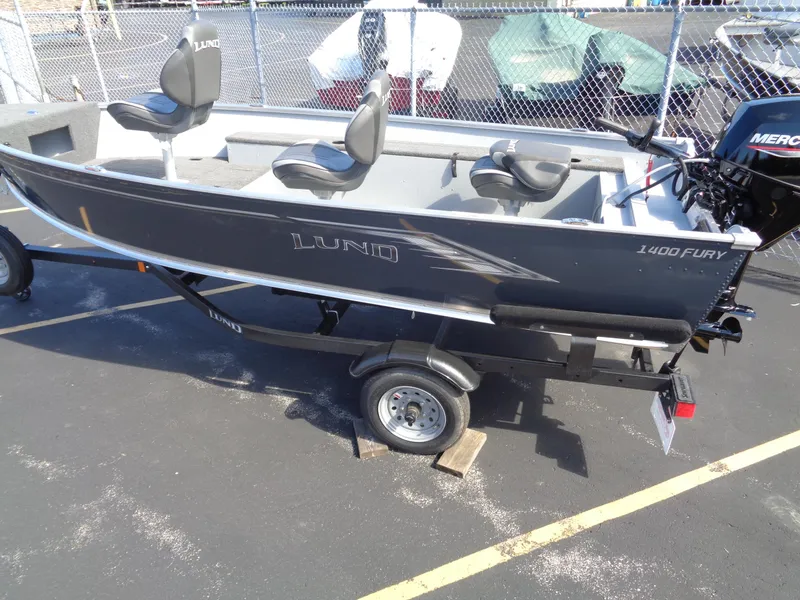 The Image of 2025 Lund 1400 Fury Tiller boat on trailer, featuring three seats and a Mercury outboard motor. - 0