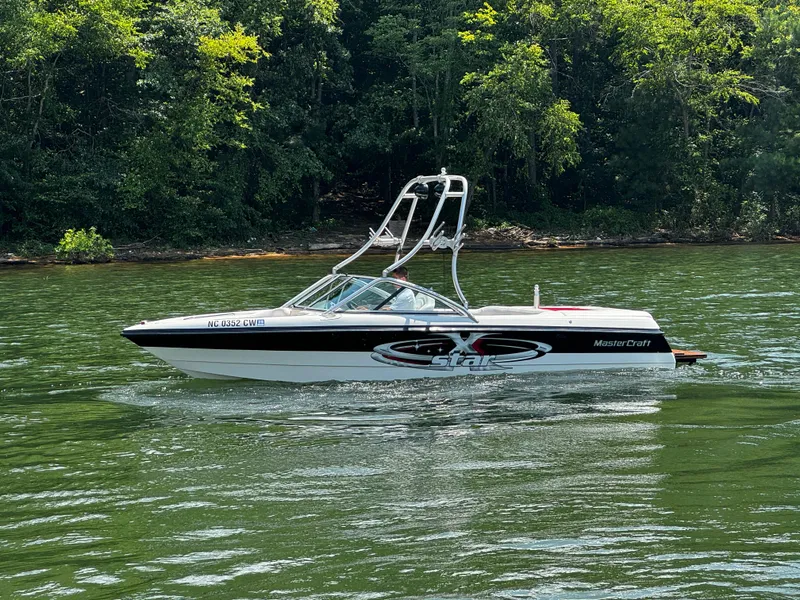Slide: The Image of 2001 MasterCraft X-Star boat cruising on a lake with lush green forest backdrop. - 7