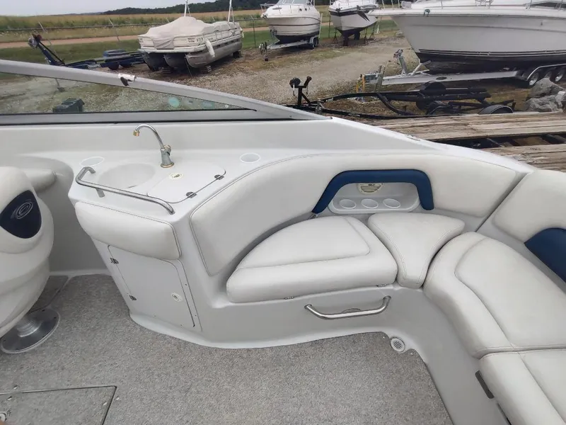 Slide: The Image of 2005 Crownline 270 BR boat interior with white seating and sink, docked near other boats. - 9