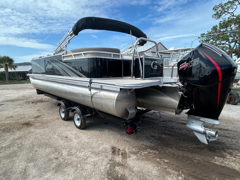 Slide: The Image of 2024 Tahoe Pontoon 2385 TZ boat with outboard motor on trailer, parked outdoors. - 3