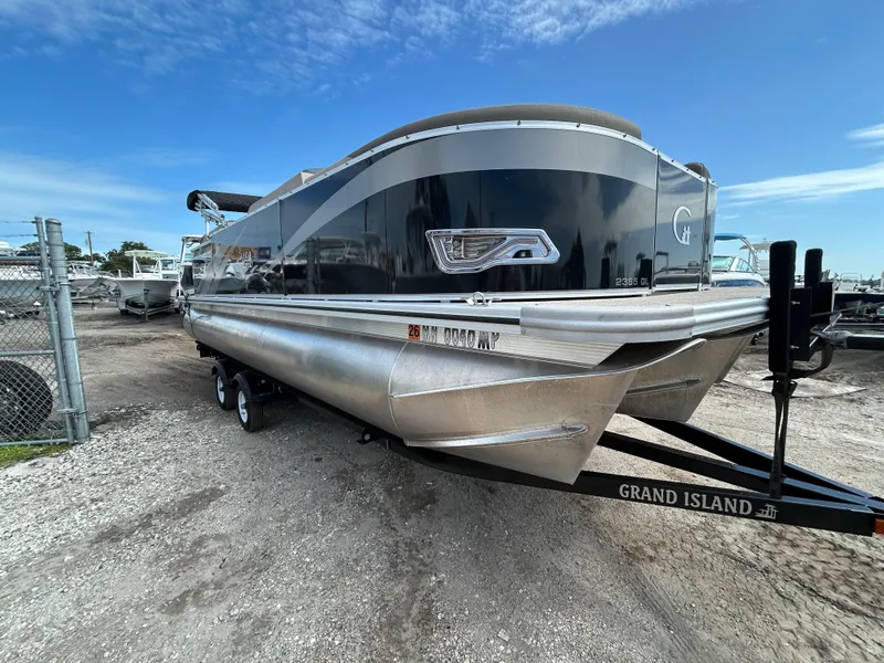 Slide: The Image of 2024 Tahoe Pontoon 2385 TZ boat on trailer, parked outdoors under blue sky. - 6