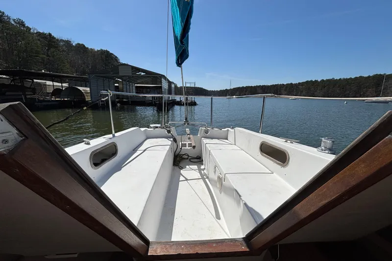 Slide: The Image of 1983 Catalina 25 sailboat cockpit view, docked on a serene lake with forested shoreline. - 24