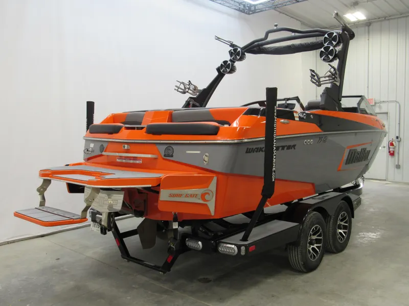 Slide: The Image of 2021 Malibu Wakesetter 22 LSV boat in orange and gray, parked indoors on a trailer. - 2