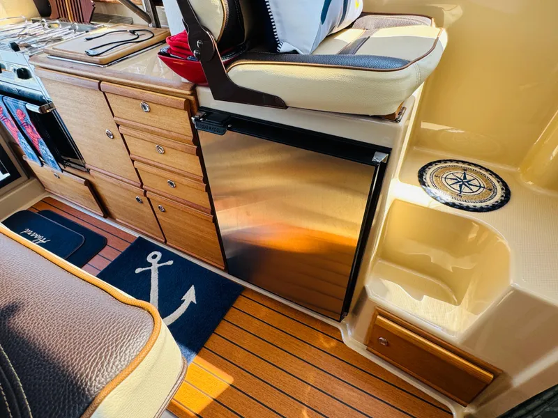 Slide: The Image of 2018 Ranger Tugs R-27 interior with wood cabinetry, compact fridge, and nautical-themed decor. - 5