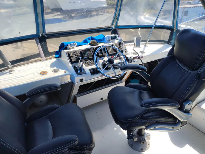 Slide: The Image of 1986 Bayliner 3870 Motoryacht helm with steering wheel, controls, and two black captain chairs. - 6