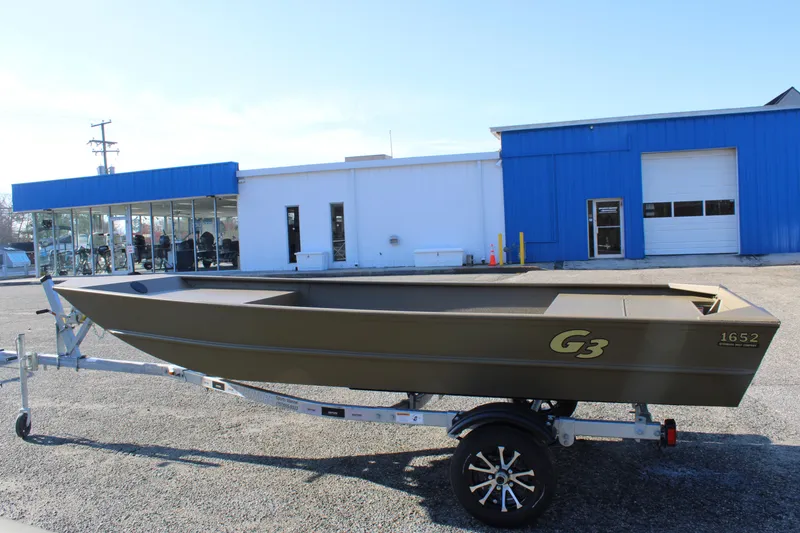 Slide: The Image of 2025 G3 Gator Tough 1652 VBW boat on trailer, parked outside a blue and white building. - 3
