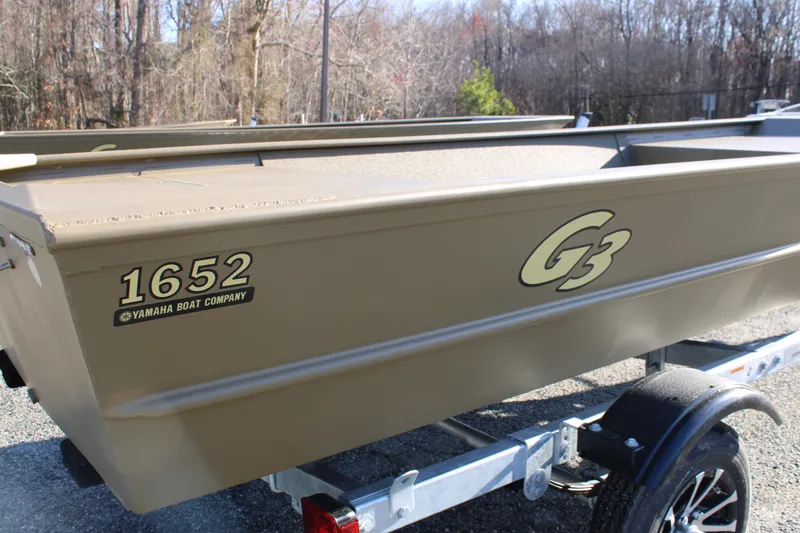 Slide: The Image of 2025 G3 Gator Tough 1652 VBW boat on trailer, outdoors in wooded area. - 7