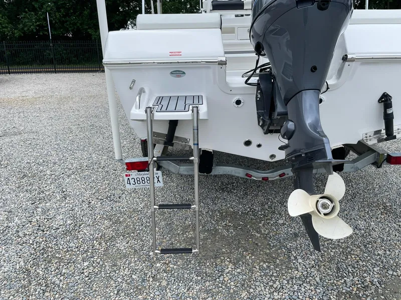 Slide: The Image of 2024 Tidewater 198 CC Adventure boat rear view with motor and ladder on gravel. - 36