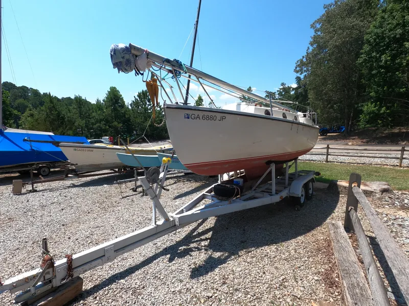 Slide: The Image of 1980 Com-Pac 23 sailboat on trailer, parked outdoors, surrounded by trees and other boats. - 3