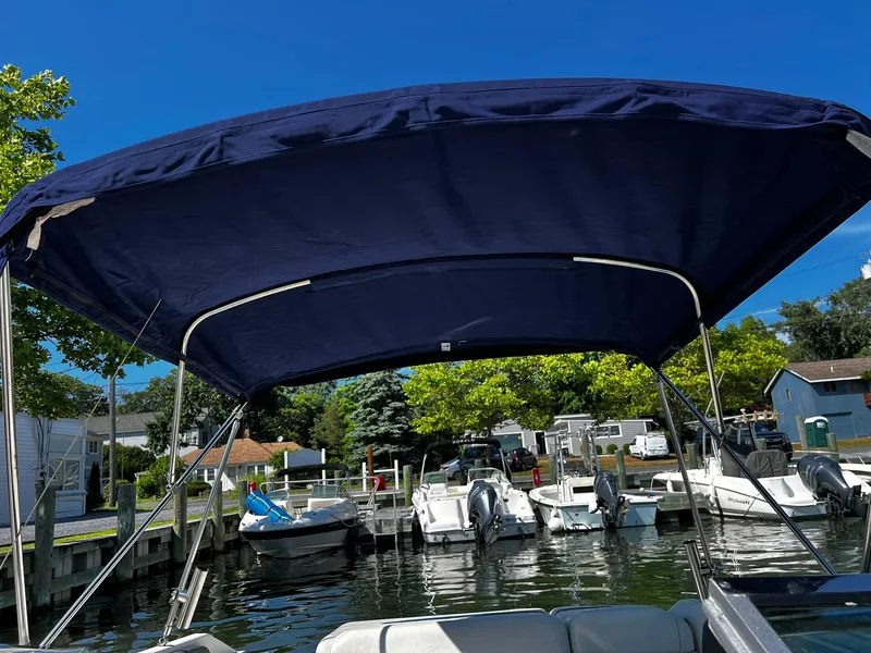 Slide: The Image of 2008 Regal 2200 Bowrider with blue canopy docked at marina under clear sky. - 19