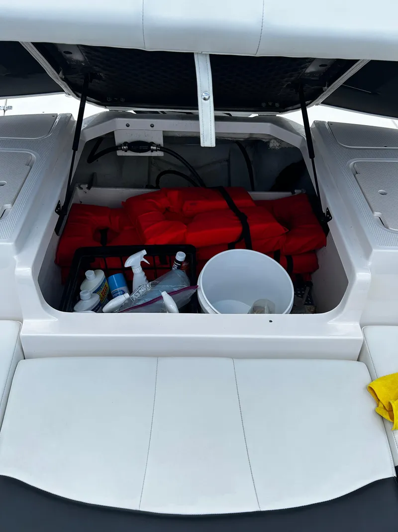Slide: The Image of Open storage compartment in 2018 Chaparral 21 H2O Sport OB with life jackets and cleaning supplies. - 32