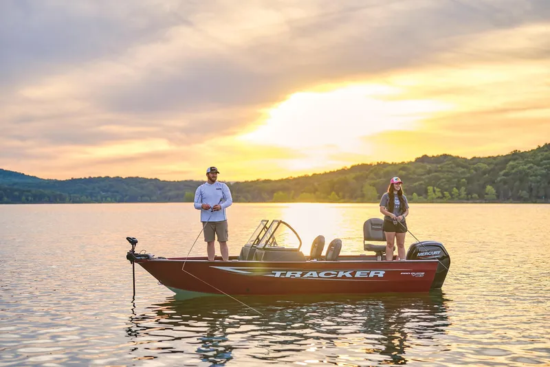 Slide: The Image of 2026 Tracker Pro Guide V-16 WT boat on a serene lake at sunset with two people fishing. - 15