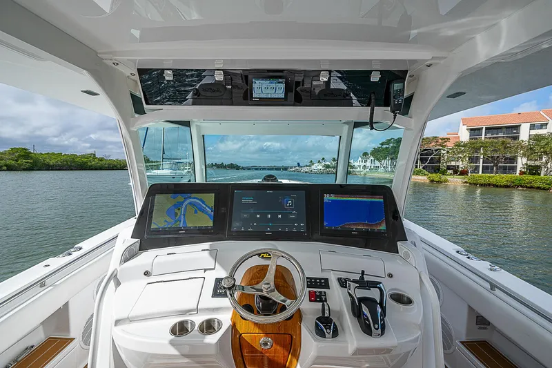 Slide: The Image of 2022 HCB 53 boat helm with advanced navigation screens and controls on a scenic waterway. - 6