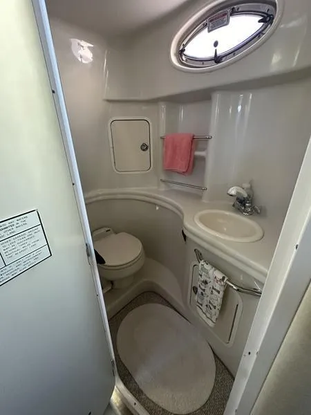 Slide: The Image of Compact bathroom in a 2007 Sea Ray 300 Sundancer boat, featuring a toilet, sink, and porthole. - 6