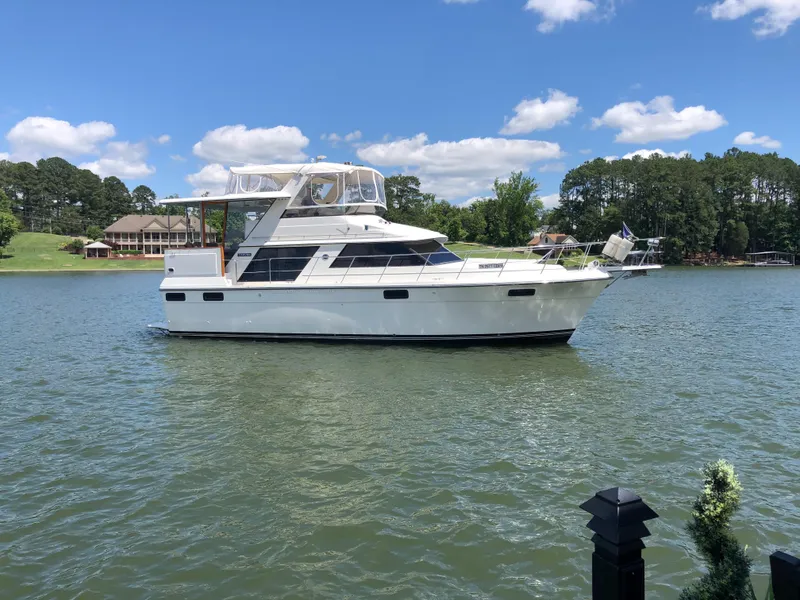 The Image of 1988 Carver 4207MY yacht on a serene lake with blue skies and lush greenery. - 0