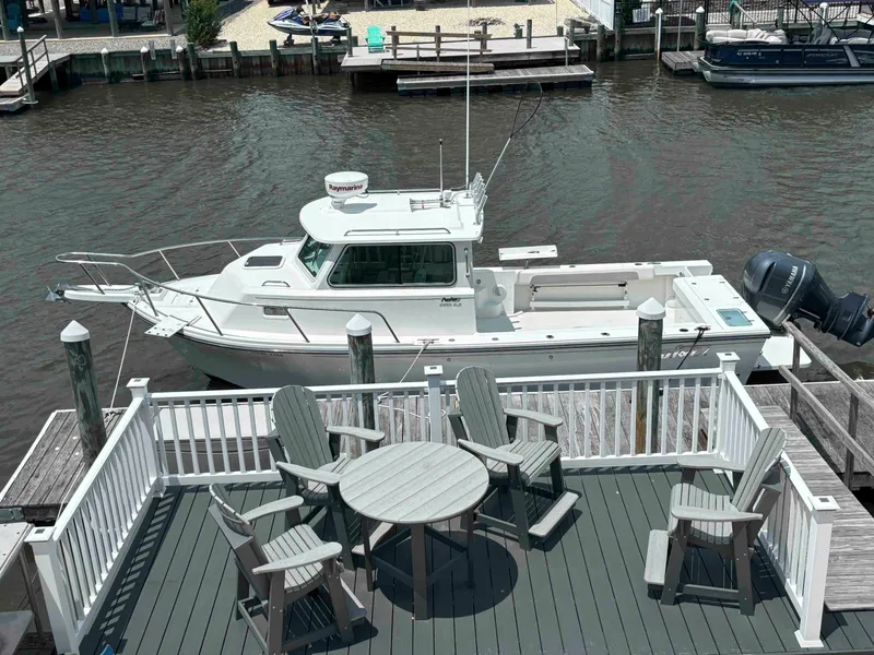 Slide: The Image of 2021 Parker 2520 XLD Sport Cabin boat docked near waterfront deck with chairs. - 2