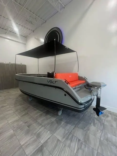 Slide: The Image of 2024 Vision Marine Technologies Volt 180 boat with canopy and orange seating in showroom. - 5