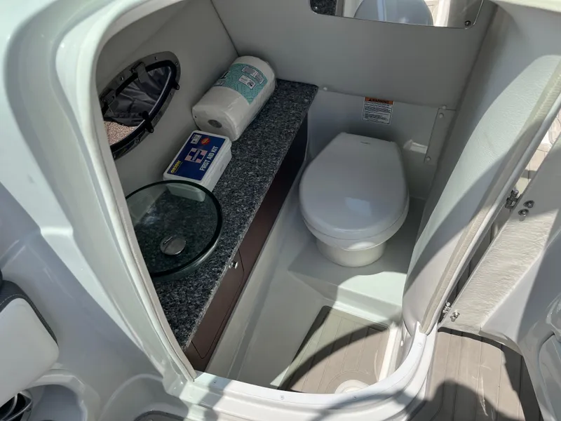 Slide: The Image of 2022 Crownline 280 SS boat bathroom with toilet, sink, and storage shelf. - 13