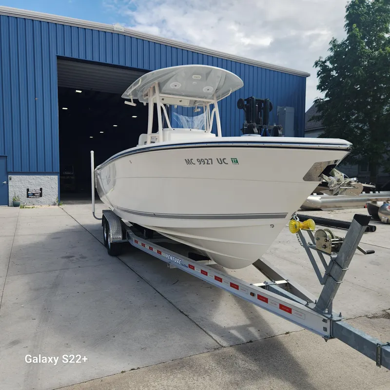 Slide: The Image of 2018 Cobia 261 Center Console boat on trailer outside blue warehouse. - 0