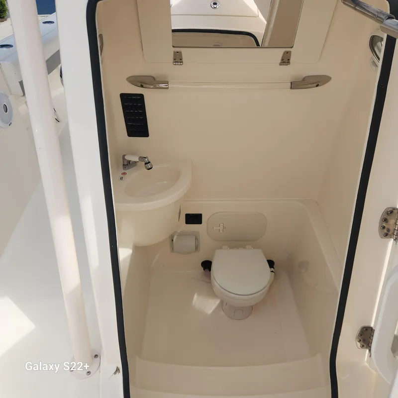 Slide: The Image of 2018 Cobia 261 Center Console boat interior with compact bathroom, featuring a toilet and sink. - 19