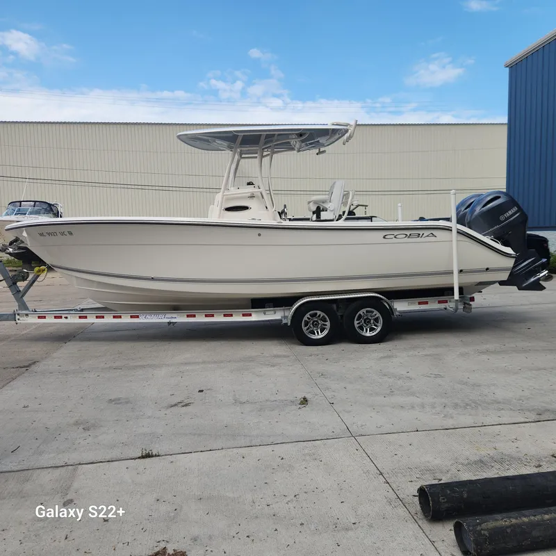 Slide: The Image of 2018 Cobia 261 Center Console boat on trailer, parked outdoors, clear sky background. - 2
