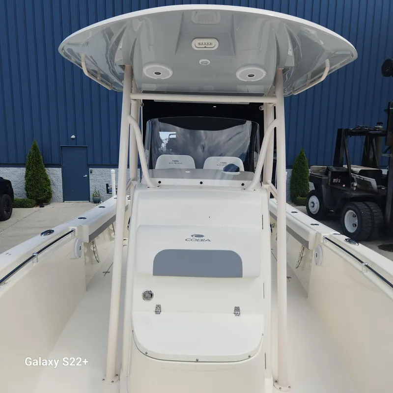 Slide: The Image of 2018 Cobia 261 Center Console boat, white exterior, docked near blue building. - 25
