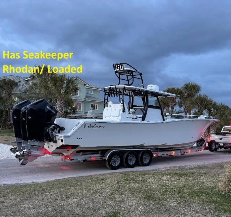 Slide: The Image of 2024 Onslow Bay 37 boat on trailer, parked near palm trees and houses. - 4