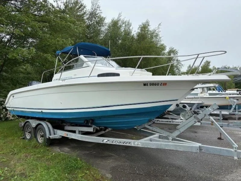 Slide: The Image of 1995 Wellcraft 238 Coastal boat on trailer, parked outdoors with trees in background. - 3