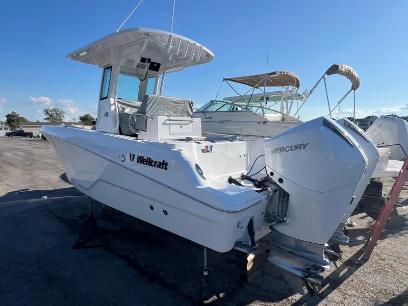 Slide: The Image of 2026 Wellcraft 243 Fisherman boat with Mercury engine, parked outdoors under clear blue sky. - 6