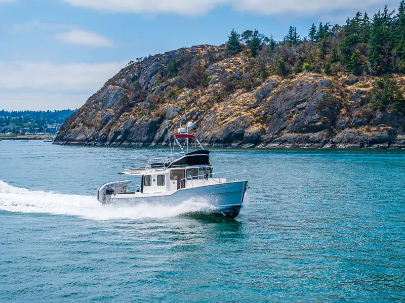 Slide: The Image of 2021 Ranger Tugs R-31 CB cruising near rocky coastline under clear skies. - 2
