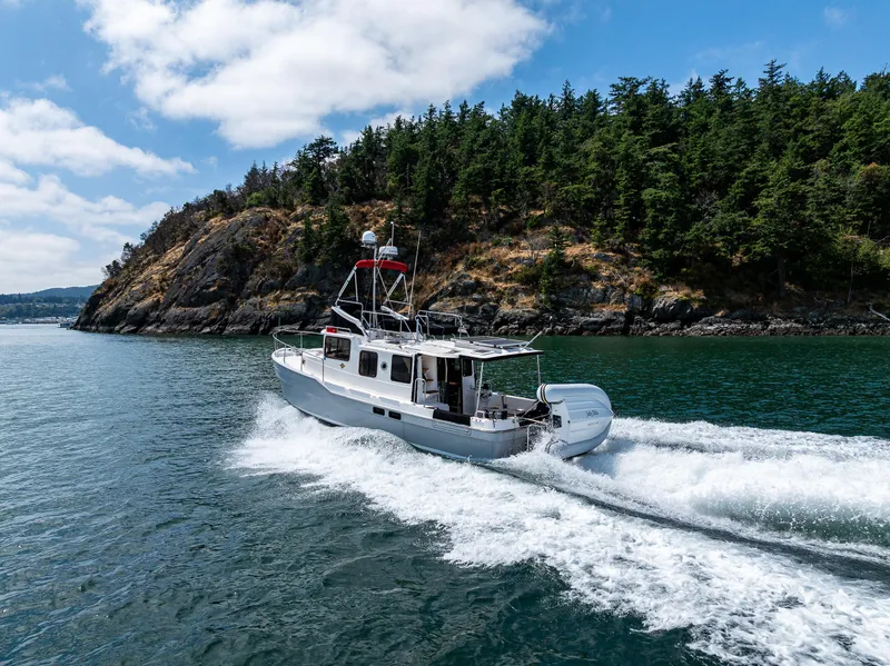 Slide: The Image of 2021 Ranger Tugs R-31 CB cruising near a forested coastline under a partly cloudy sky. - 4