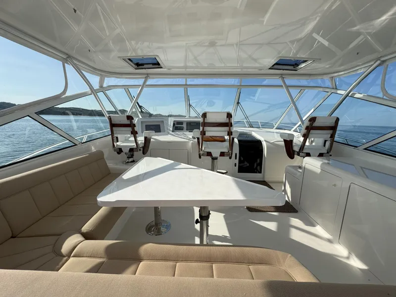 Slide: The Image of 2007 Viking 52 Open yacht interior with seating, table, and helm chairs on a sunny day. - 17
