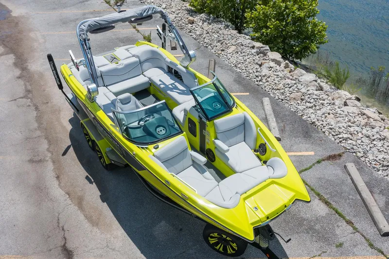 Slide: The Image of 2018 MasterCraft X23 boat, vibrant yellow, parked near a lake with plush seating and sleek design. - 1