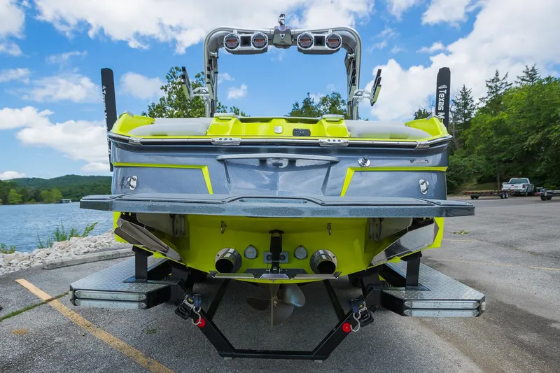 Slide: The Image of 2018 MasterCraft X23 boat, rear view, parked near a scenic lake with trees and blue sky. - 18