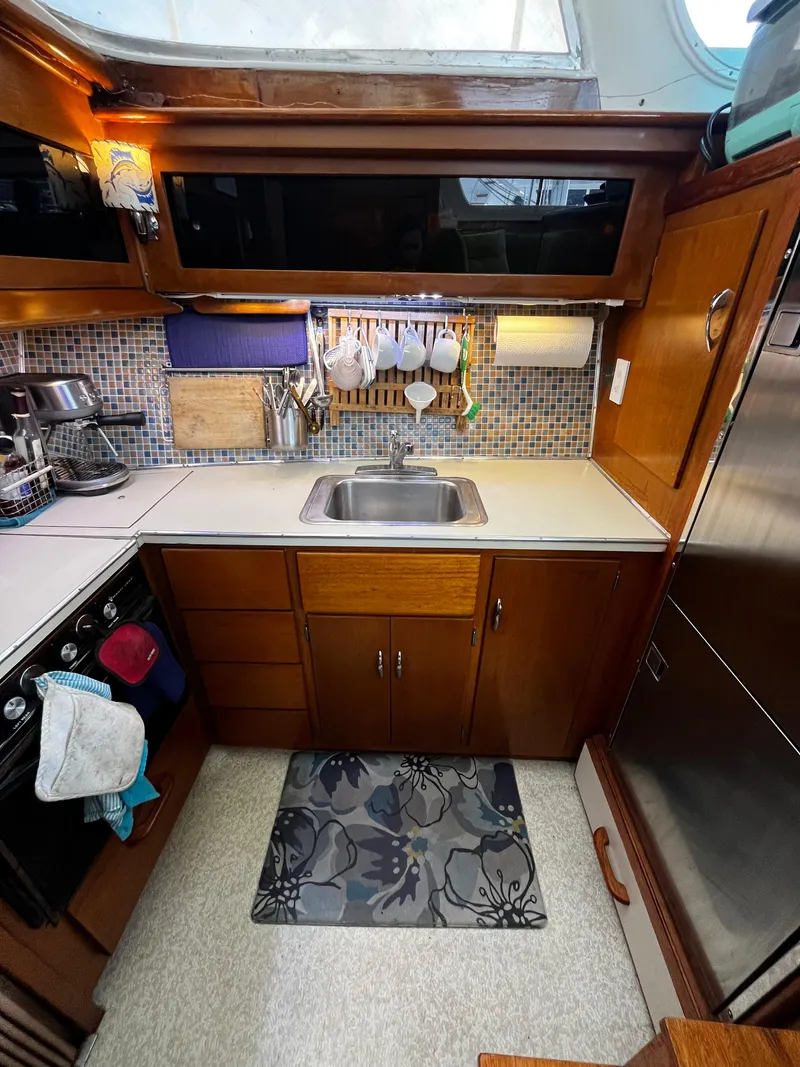 Slide: The Image of Compact kitchen in a 1965 Hatteras 41 Twin Cabin yacht, featuring wood cabinets and a stainless steel sink. - 29