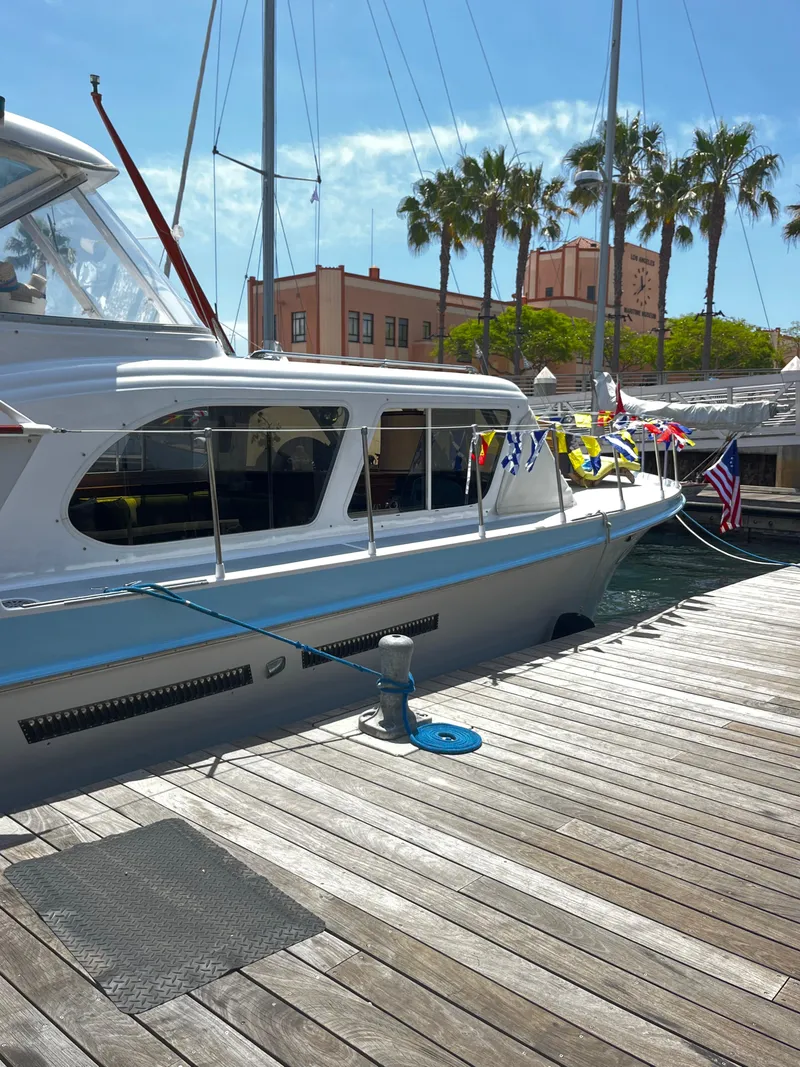 Slide: The Image of 1965 Hatteras 41 Twin Cabin yacht docked, adorned with colorful flags, palm trees in background. - 4