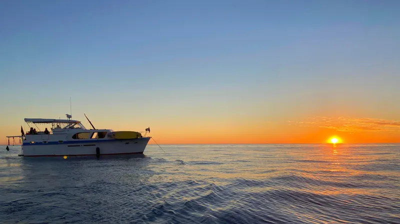 Slide: The Image of 1965 Hatteras 41 Twin Cabin yacht at sunset on calm ocean waters. - 47