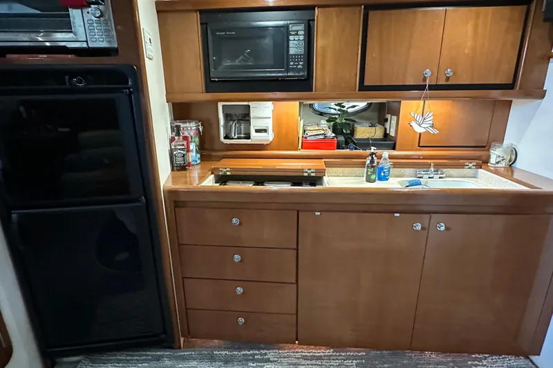 Slide: The Image of 1998 Trojan 440 Express yacht kitchen with microwave, fridge, and wooden cabinetry. - 12