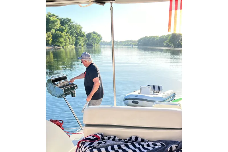 Slide: The Image of Man grilling on a 1998 Trojan 440 Express boat, serene river backdrop. - 29