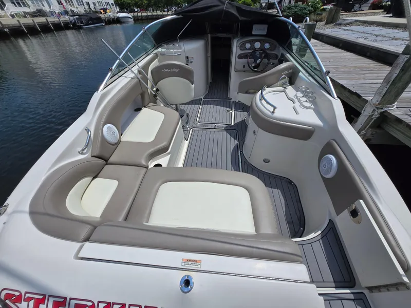 Slide: The Image of 2006 Sea Ray 270 Sundeck interior with beige seating and modern dashboard, docked by the water. - 1