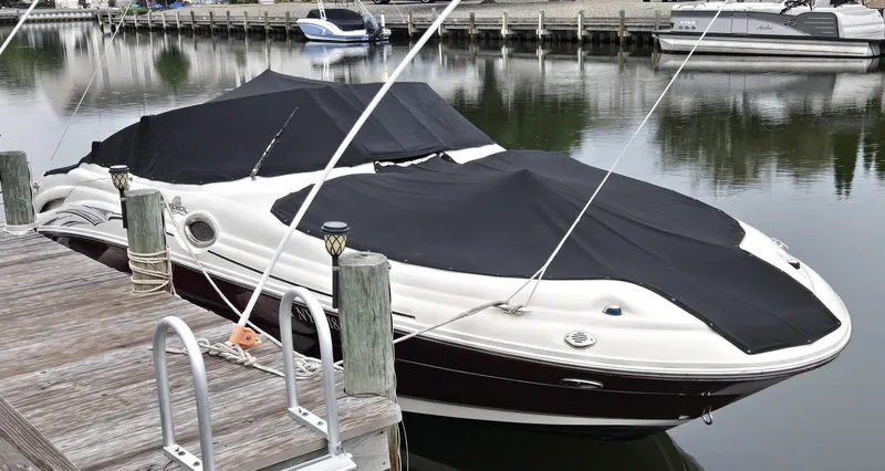 Slide: The Image of 2006 Sea Ray 270 Sundeck boat docked with black cover, calm water reflection. - 10