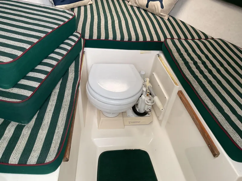 Slide: The Image of 1997 Pursuit 2460 Denali boat interior with striped cushions and compact marine toilet. - 10