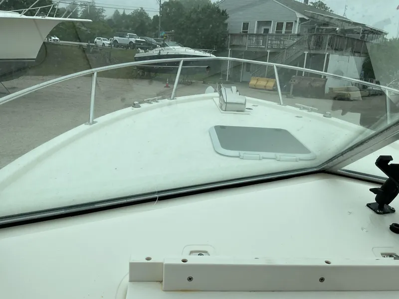 Slide: The Image of 1997 Pursuit 2460 Denali boat view from cockpit, docked near a house and parked cars. - 4