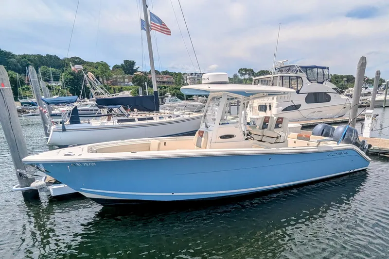 Slide: The Image of 2023 Cobia 280 Center Console boat docked in a marina, surrounded by other vessels. - 0